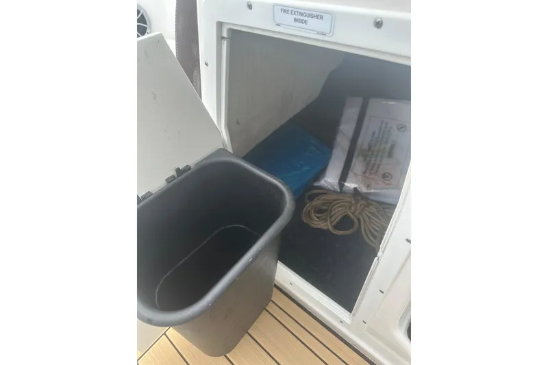Slide: The Image of Storage compartment on 2021 Yamaha Boats 195S with fire extinguisher, rope, and trash bin. - 13