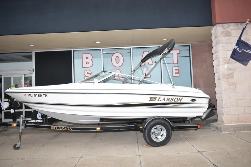 The Image of 2004 Larson SEi 180 boat on trailer, displayed for sale outside dealership. - 1