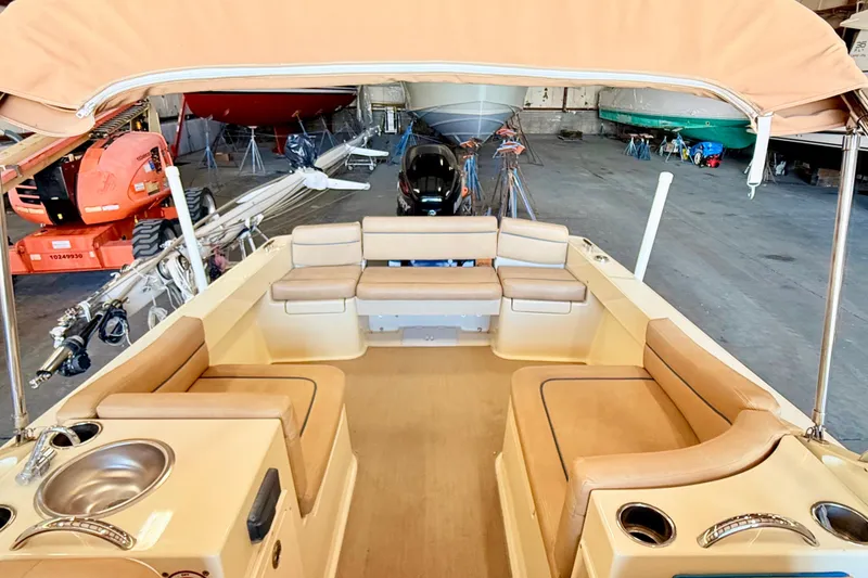 Slide: The Image of 2018 Vanquish Bristol Harbor 23 boat interior with tan seating and canopy in a storage facility. - 8