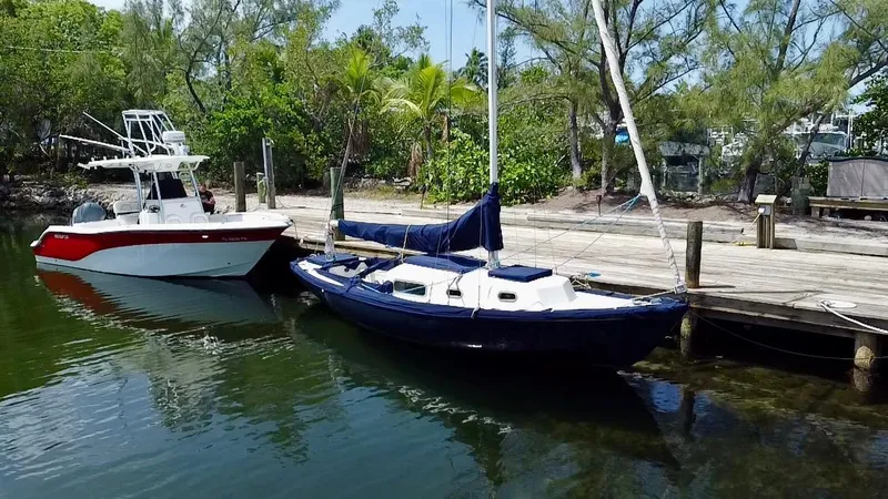 Slide: The Image of 1968 Sailboat 24 docked beside a motorboat, surrounded by lush greenery. - 4
