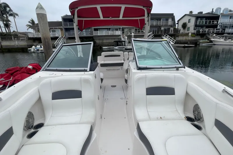 Slide: The Image of 2014 Chaparral 224 Sunesta boat with white seating and red canopy docked by waterfront homes. - 13