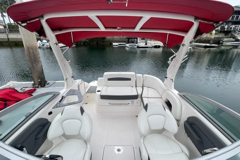 Slide: The Image of 2014 Chaparral 224 Sunesta boat interior with red canopy, docked by calm water. - 15