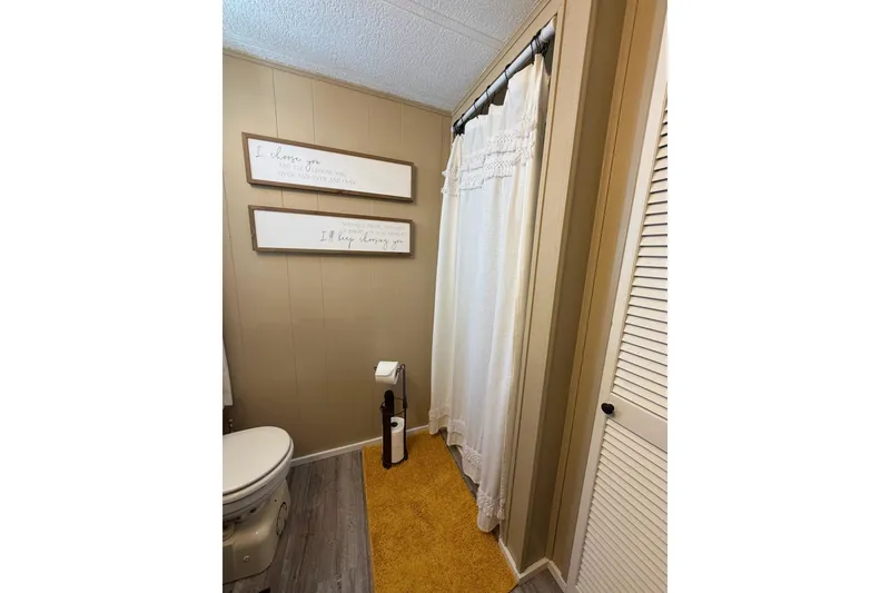 Slide: The Image of Bathroom with beige walls, white shower curtain, and motivational wall art in a 1988 STARDUST 16x70. - 24