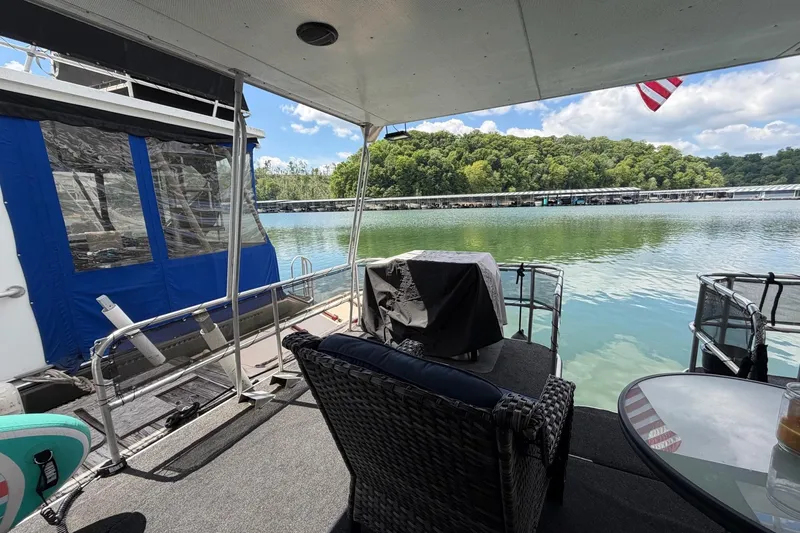 Slide: The Image of Houseboat deck view with wicker chair, table, and scenic lake backdrop. STARDUST 16x70, 1988 model. - 35