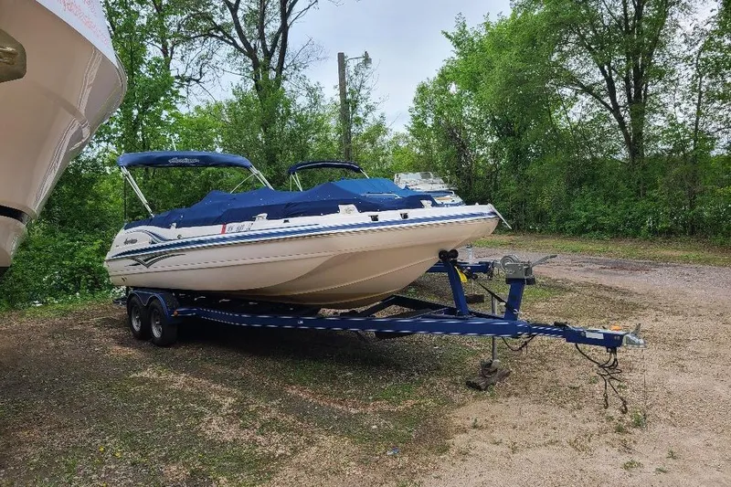 The Image of 2006 Hurricane SunDeck 257 DC IO boat on trailer, parked outdoors with trees in background. - 0