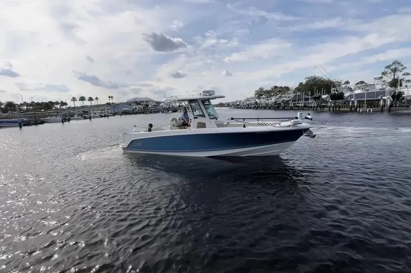 The Image of 2024 Boston Whaler 280 Outrage cruising on a calm waterway under a partly cloudy sky. - 1