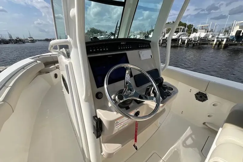 Slide: The Image of 2024 Boston Whaler 280 Outrage boat helm with steering wheel and controls, docked by the water. - 11