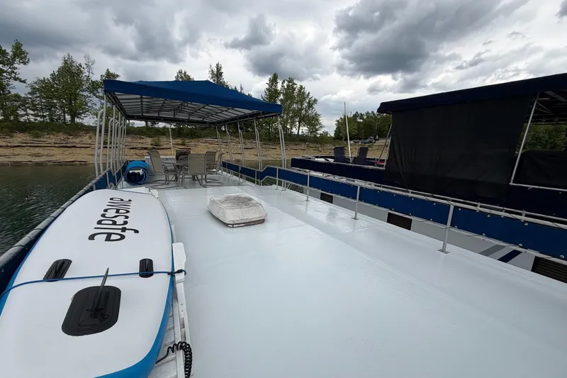 Slide: The Image of 1987 Jamestowner 14x60 houseboat with deck seating and paddleboard, under cloudy skies. - 27