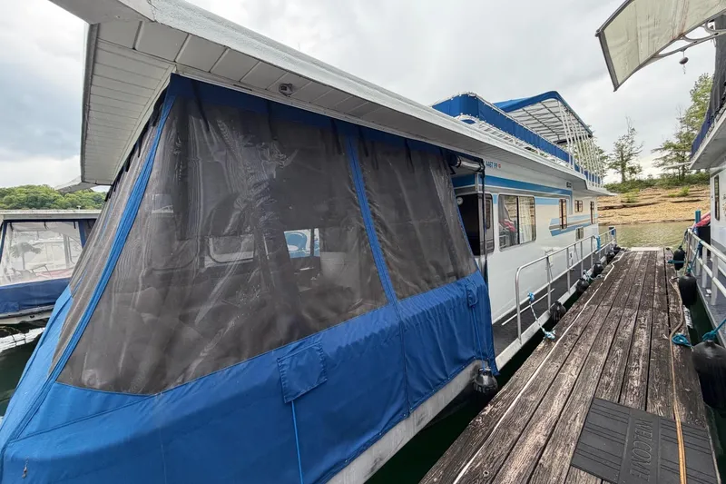 Slide: The Image of 1987 Jamestowner 14x60 houseboat docked, featuring blue canvas enclosure and wooden walkway. - 32