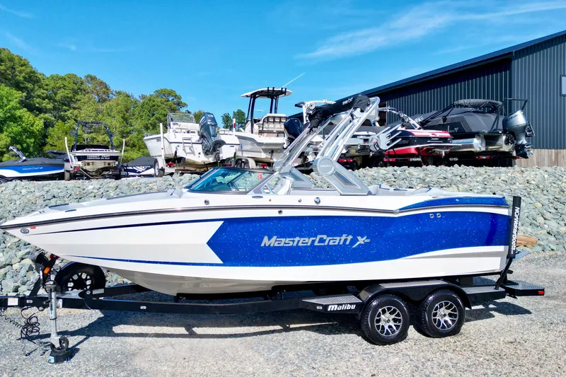 The Image of 2022 MasterCraft XStar boat in blue and white, parked on a trailer outdoors. - 0