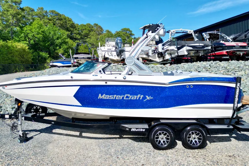 Slide: The Image of 2022 MasterCraft XStar boat in blue and white on a trailer, surrounded by trees and other boats. - 1