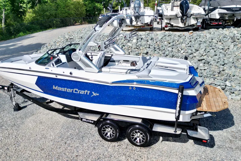 Slide: The Image of 2022 MasterCraft XStar boat on trailer, blue and white design, parked outdoors. - 2