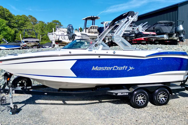 Slide: The Image of 2022 MasterCraft XStar boat on trailer, blue and white design, parked outdoors. - 4