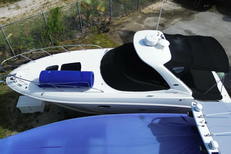 Slide: The Image of 2003 Monterey 302 Cruiser boat with black canopy and blue cover, parked near a fence. - 8