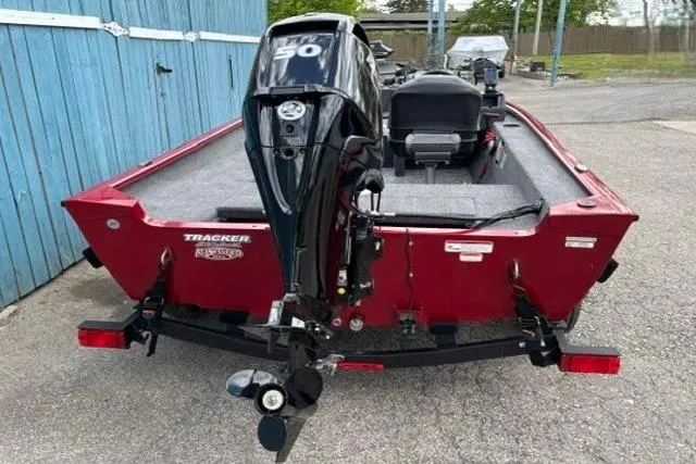 Slide: The Image of Red 2025 Tracker Super Guide V-16 SC boat with outboard motor, parked near blue fence. - 3
