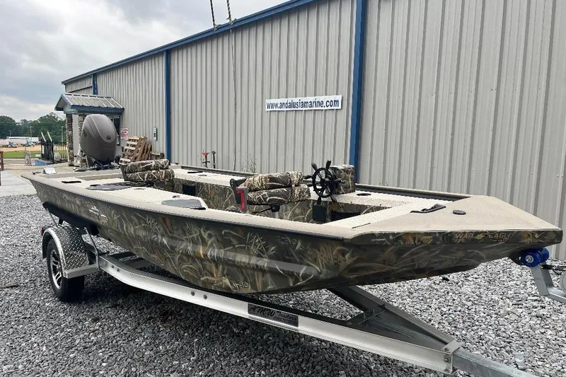 Slide: The Image of 2026 War Eagle 754VS Stick Steer boat on trailer, camo design, parked outside a marine shop. - 4