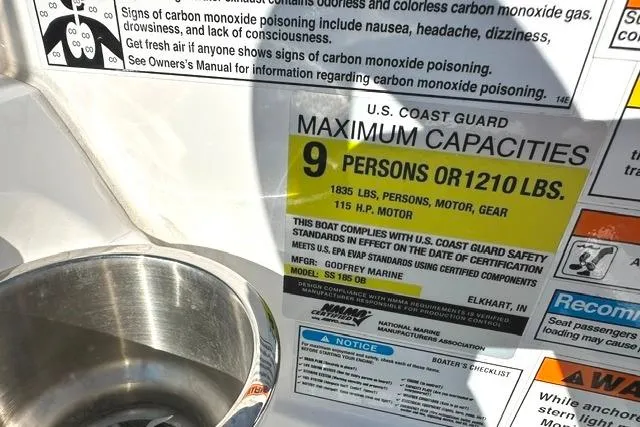 Slide: The Image of 2021 Hurricane SunDeck Sport 185 OB capacity label, 9 persons or 1210 lbs, safety warnings visible. - 15
