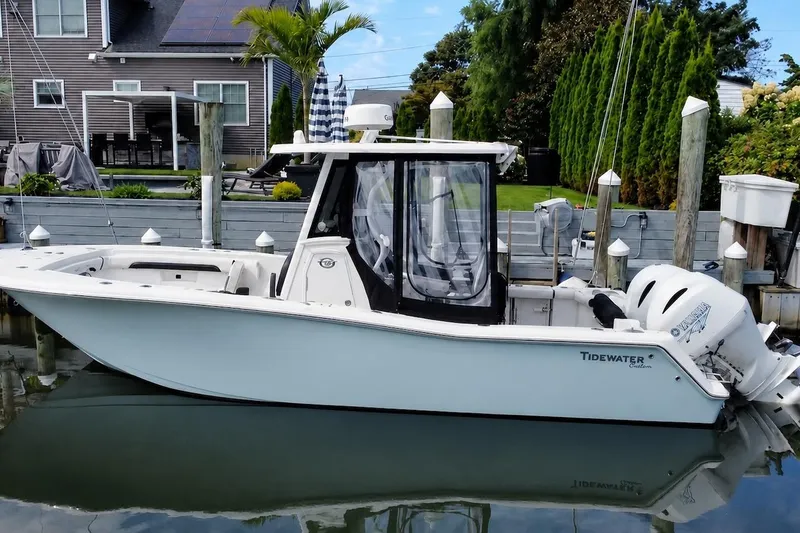 The Image of 2021 Tidewater 256 CC Adventure boat docked by a modern waterfront home. - 0