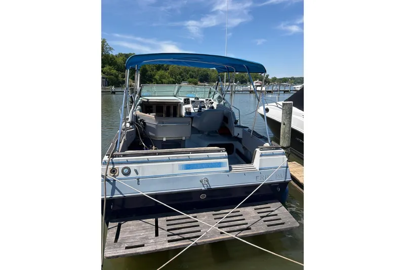 Slide: The Image of 1987 Four Winns 245 Vista boat docked, featuring blue canopy and spacious deck. - 3