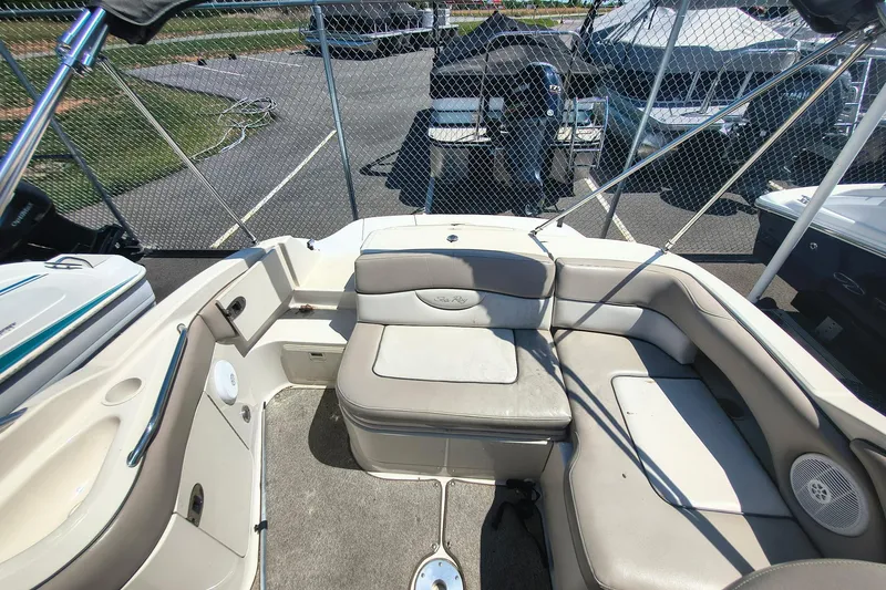 Slide: The Image of 2004 Sun Deck 220 boat interior with cushioned seating and speaker, parked near other boats. - 6