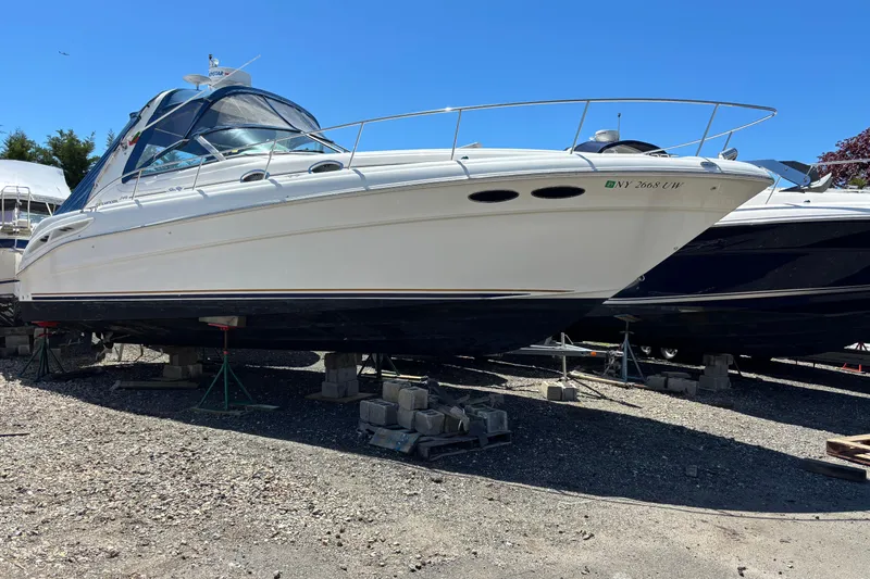 The Image of 2000 Sea Ray 340 Sundancer yacht on dry dock, white hull, clear blue sky background. - 0