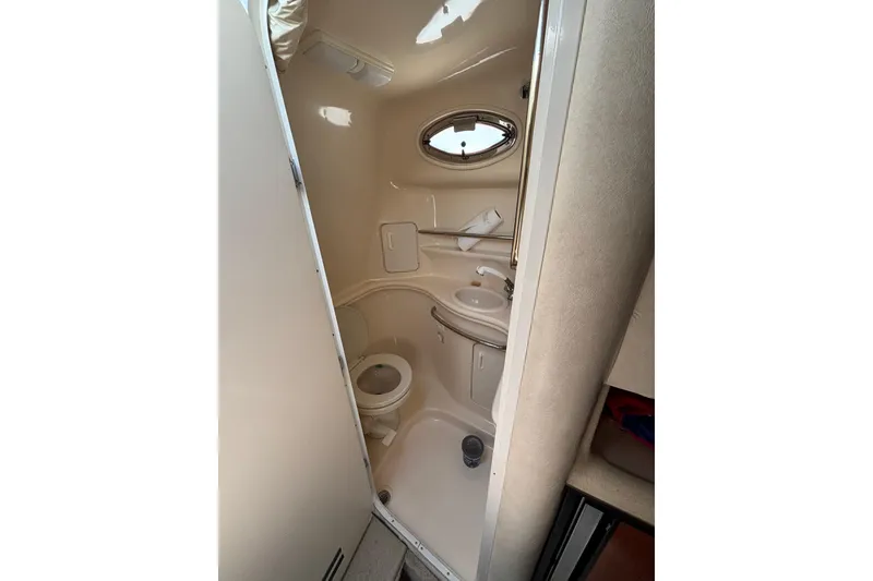 Slide: The Image of Compact bathroom in 2000 Sea Ray 340 Sundancer yacht, featuring toilet, sink, and porthole window. - 12