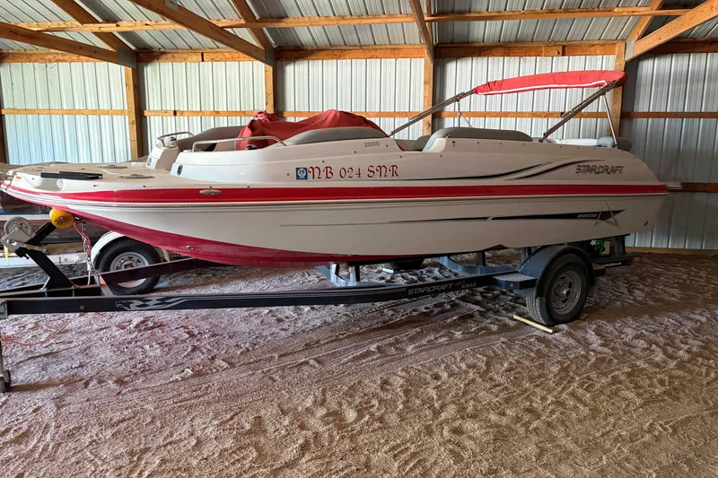 The Image of 2013 Starcraft 2000 IO Limited boat in storage, red and white design, on trailer. - 0
