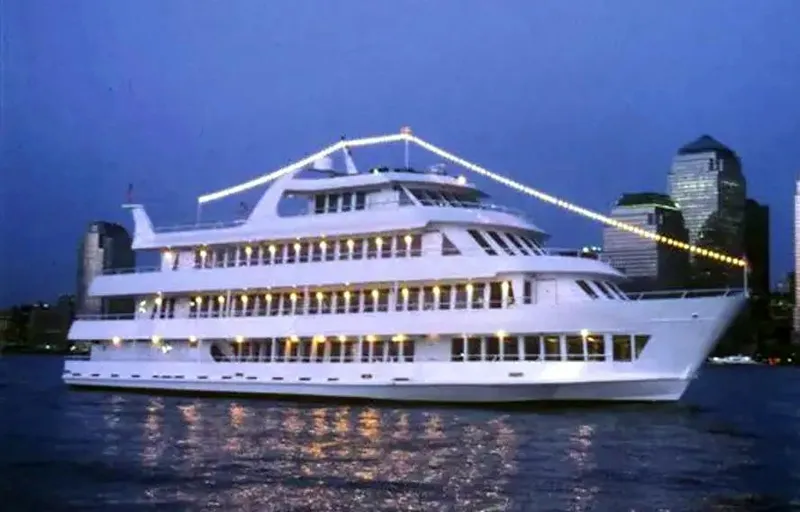 Slide: The Image of Blount 130 Dinner Cruise yacht illuminated at night on the water, city skyline in background. - 3