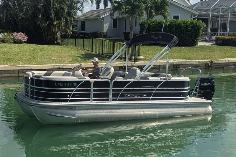 The Image of 2021 Trifecta 22RF LE pontoon boat on a calm waterway, featuring a Suzuki outboard motor. - 1