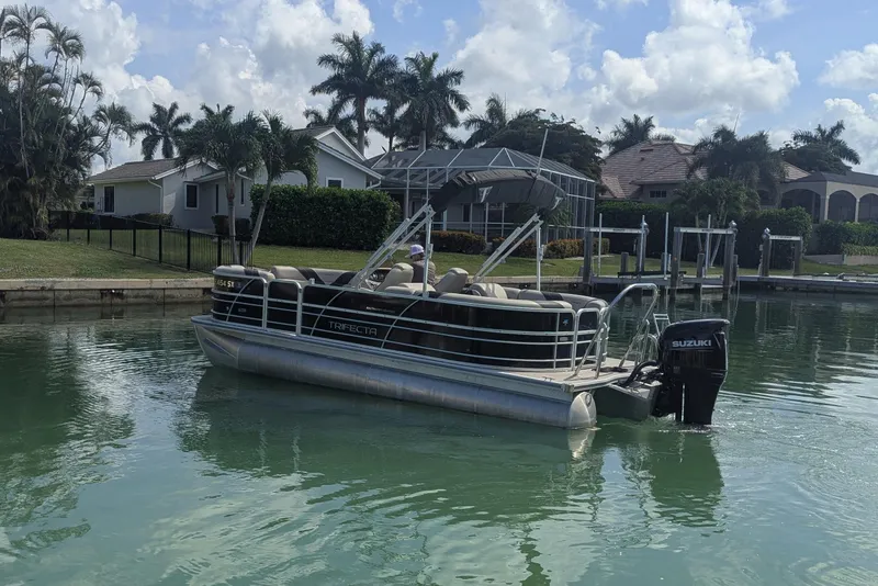 Slide: The Image of 2021 Trifecta 22RF LE pontoon boat docked on a serene waterfront with palm trees. - 2