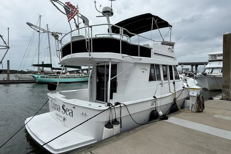 Slide: The Image of 1998 Mainship 350 Trawler docked at marina, overcast sky, American flag visible. - 3