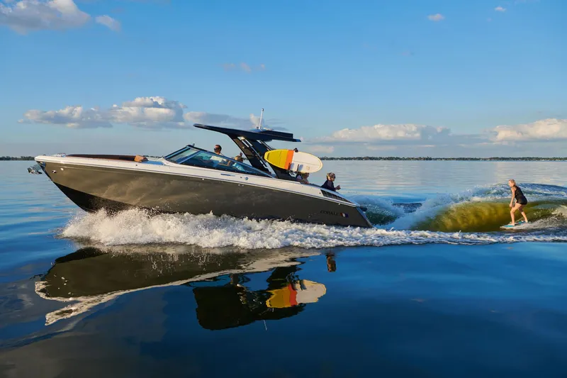 Slide: The Image of Manufacturer Provided Image: 2025 Cobalt R33 Surf boat on water with wakeboarder, sunny day, clear sky. - 23