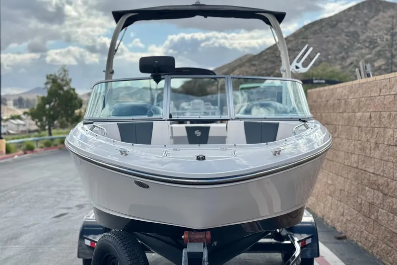 Slide: The Image of 2020 Chaparral 21 Surf boat on trailer, parked near a brick wall with mountains in background. - 2