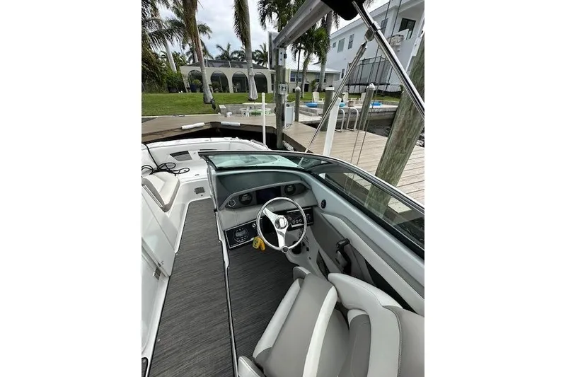 Slide: The Image of 2020 Four Winns HD220 OB boat interior with steering wheel and seating, docked near palm trees. - 13