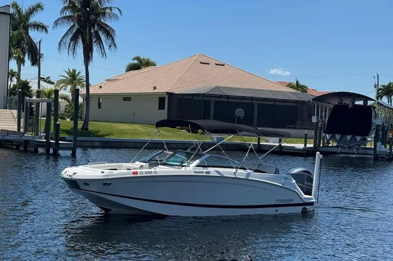 Slide: The Image of 2020 Four Winns HD220 OB boat docked on a sunny waterfront with palm trees. - 2