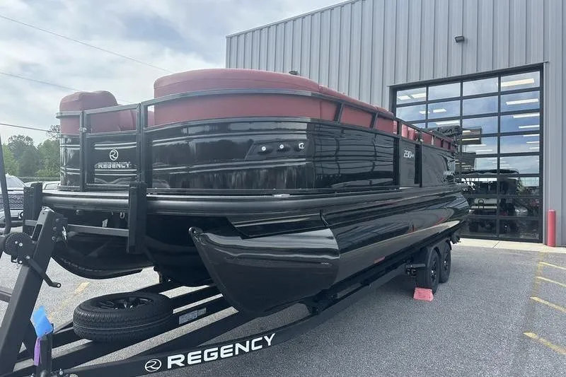 The Image of 2026 Regency 230 DL pontoon boat on trailer outside a modern building. - 0