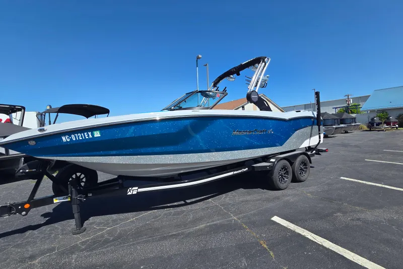 Slide: The Image of 2022 MasterCraft NXT24 boat on trailer in parking lot under clear blue sky. - 2