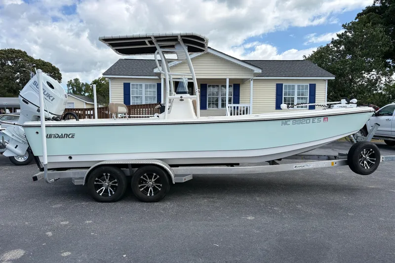 Slide: The Image of 2021 Sundance DX22 boat on trailer, parked in front of a house under a cloudy sky. - 1