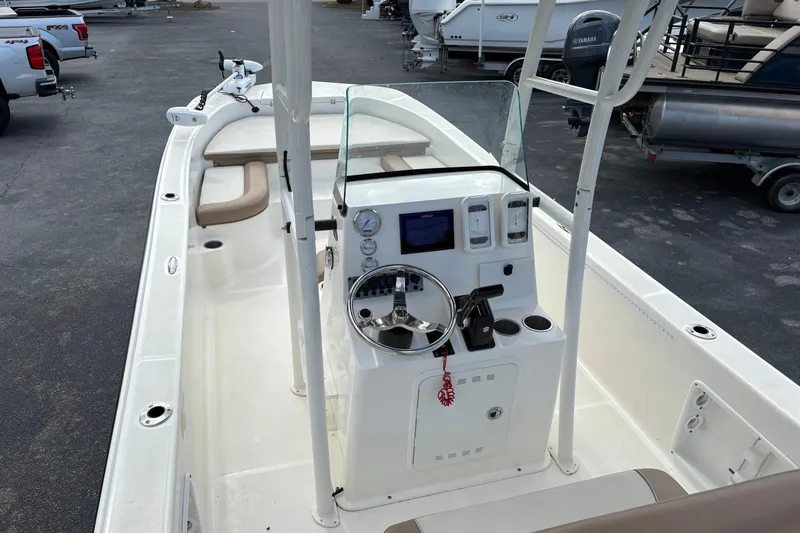 Slide: The Image of 2021 Sundance DX22 boat interior with steering console and seating, parked in a marina. - 15