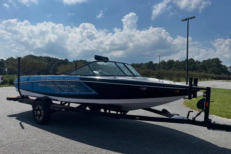 The Image of 2015 Nautique Ski Nautique 200 Open Bow boat on trailer under a cloudy sky. - 1