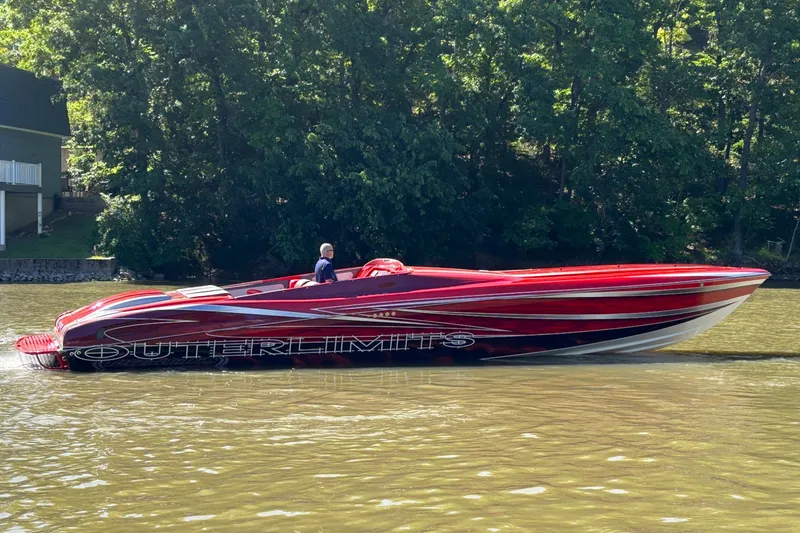 The Image of Red 2004 Outerlimits 42 Legacy speedboat cruising on a river with lush green trees. - 1