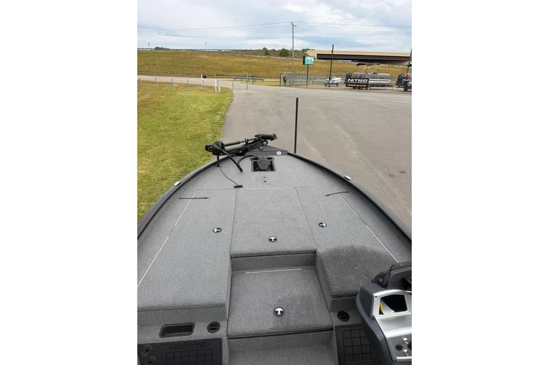 Slide: The Image of 2025 Tracker Savage 215 boat deck with trolling motor, parked on pavement near grassy area. - 5