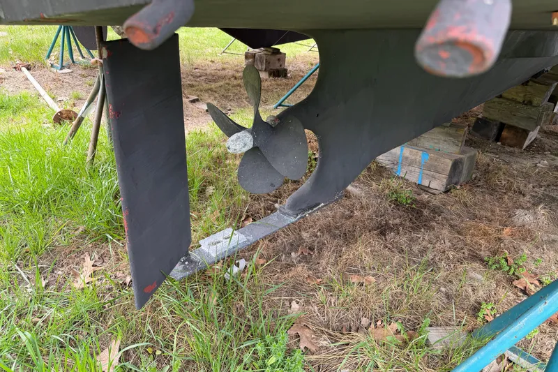 Slide: The Image of 2005 Camano Trawler propeller and rudder on dry land, surrounded by grass. - 39