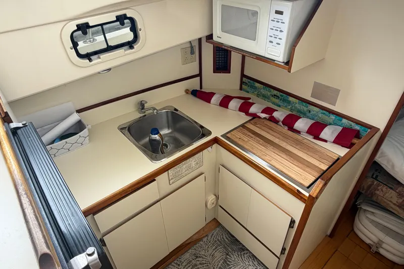 Slide: The Image of Compact kitchen area in a 2005 Camano Trawler, featuring a sink, microwave, and cutting board. - 8