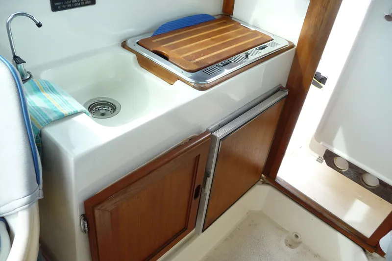 Slide: The Image of 1988 Bayliner 2102 Trophy boat interior with sink, cutting board, and wooden cabinetry. - 11