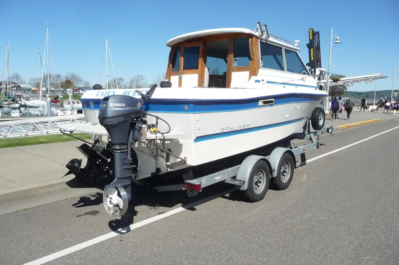 Slide: The Image of 1988 Bayliner 2102 Trophy boat on trailer, parked near marina under clear blue sky. - 5