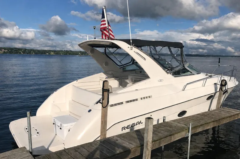 Slide: The Image of 1995 Regal Commodore 322 boat docked on a serene lake under cloudy skies. - 2