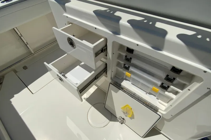 Slide: The Image of Storage compartments on a 2026 Cobia 245 Center Console boat, featuring open drawers and tackle boxes. - 17