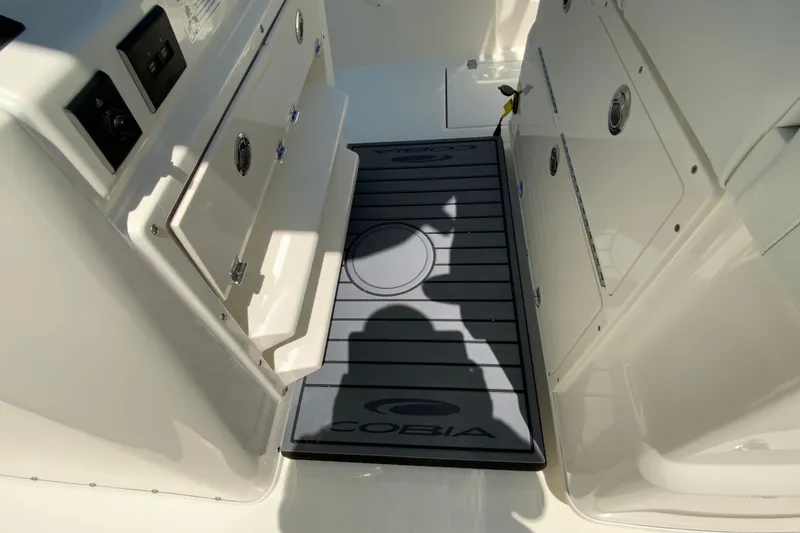 Slide: The Image of Interior view of a 2026 Cobia 245 Center Console boat, featuring storage compartments and a branded mat. - 27
