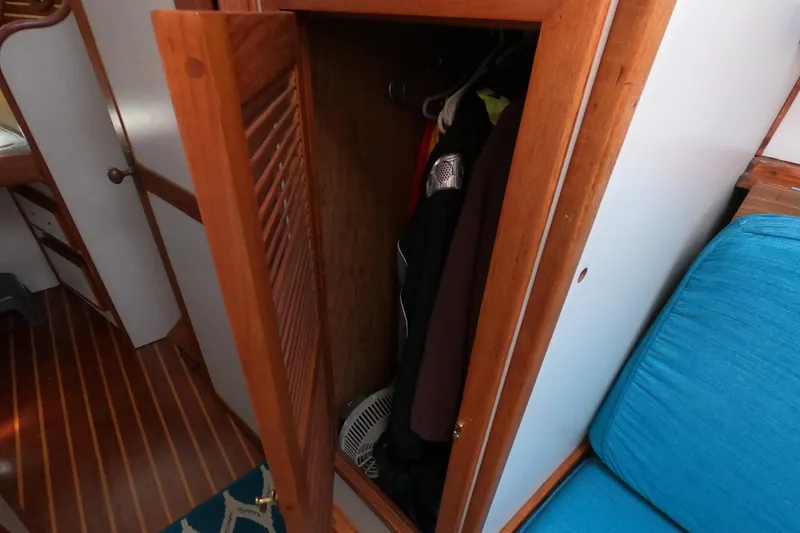 Slide: The Image of Wooden closet interior on a 1978 CSY 44 sailboat, featuring hanging clothes and a blue cushion. - 19